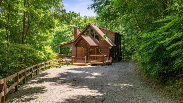 exterior space featuring a wooden deck, a forest view, gravel driveway, and a chimney