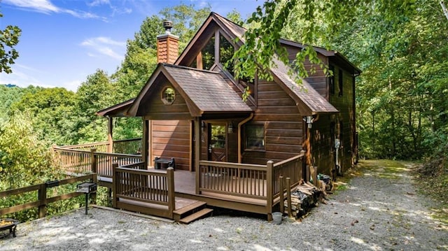 rear view of property featuring a wooden deck, a view of trees, and a chimney