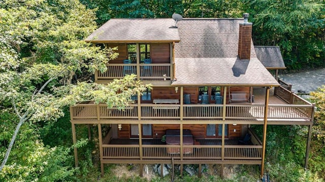 rear view of house with a wooden deck, a shingled roof, a chimney, and a balcony