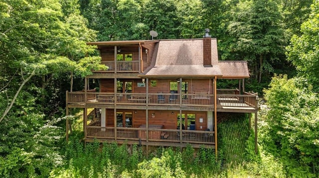 back of house featuring a wooded view, a chimney, a balcony, and a deck