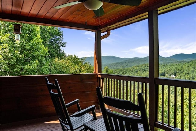 wooden deck featuring a ceiling fan, a mountain view, and a view of trees