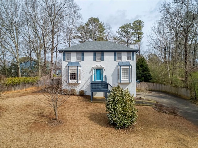 colonial home featuring a chimney and fence