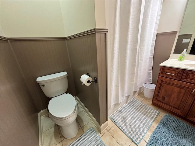 bathroom featuring tile patterned floors, shower / bathtub combination with curtain, toilet, wainscoting, and vanity