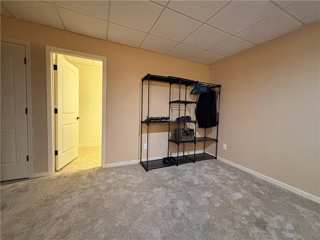 unfurnished bedroom featuring a drop ceiling, baseboards, and carpet