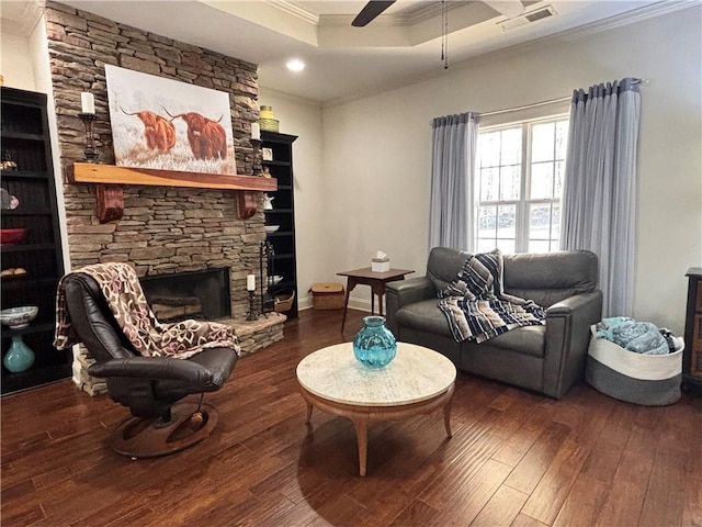 living area with visible vents, hardwood / wood-style floors, a stone fireplace, crown molding, and ceiling fan