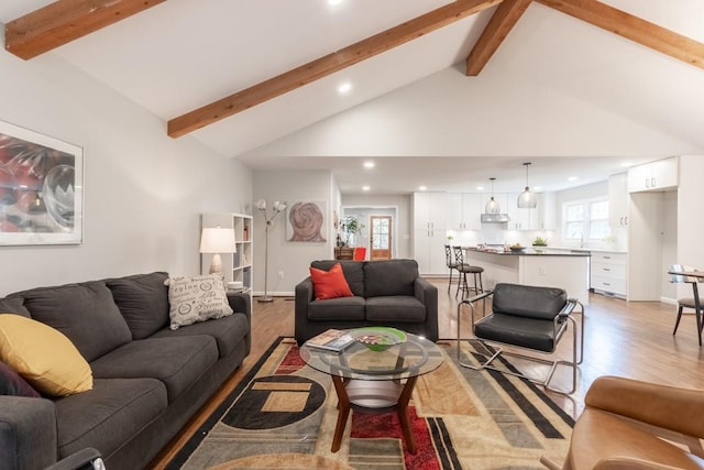 living room featuring beamed ceiling, sink, light wood-type flooring, and high vaulted ceiling