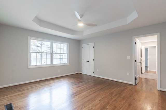 unfurnished room with hardwood / wood-style flooring, a raised ceiling, and ceiling fan