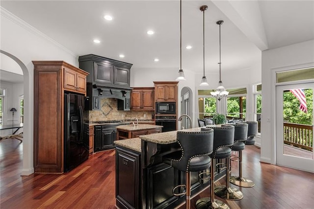 kitchen featuring black appliances, a kitchen island with sink, dark wood-type flooring, and pendant lighting