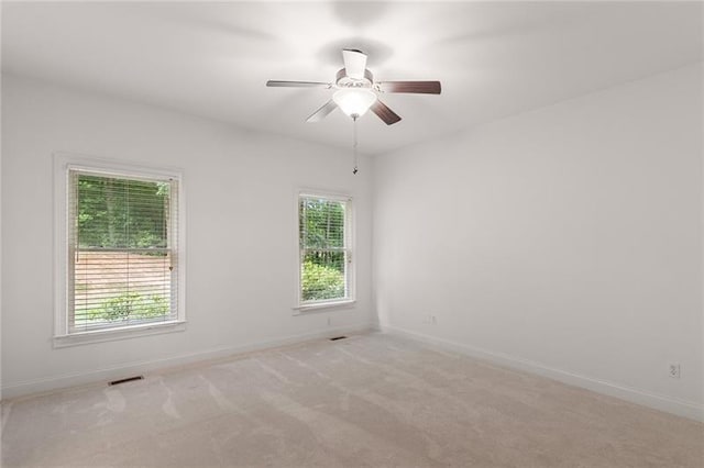 empty room featuring ceiling fan, light colored carpet, and plenty of natural light