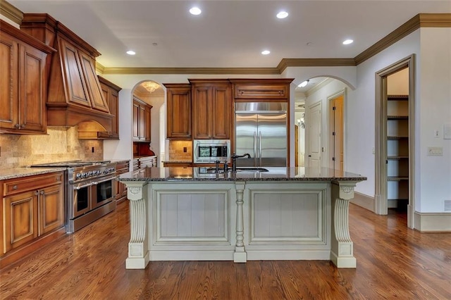 4853 Stonehall Pl, Atlanta, GA 30339 - kitchen with built in appliances, arched walkways, dark stone countertops, a center island with sink, and dark wood-type flooring