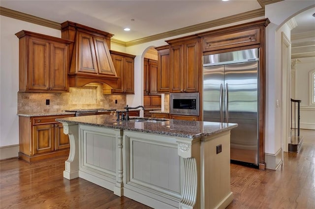 4853 Stonehall Pl, Atlanta, GA 30339 - kitchen with built in appliances, a sink, arched walkways, dark stone counters, and brown cabinetry