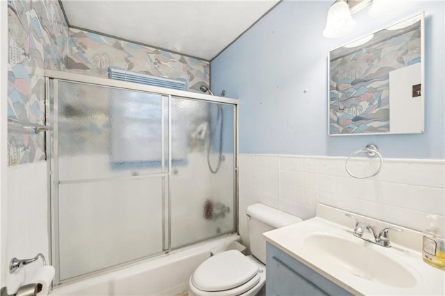 full bath with vanity, wainscoting, toilet, tile walls, and enclosed tub / shower combo