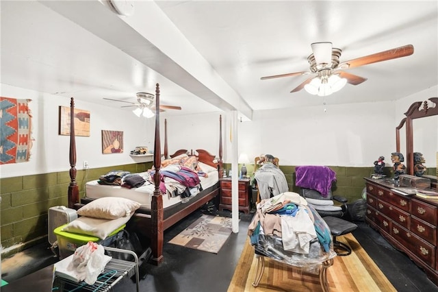 bedroom featuring concrete flooring, a ceiling fan, and wainscoting