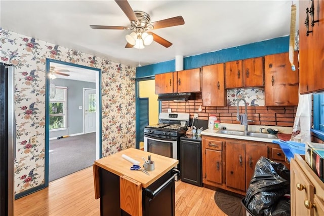 kitchen with a ceiling fan, stainless steel gas stove, wooden counters, brown cabinets, and a sink