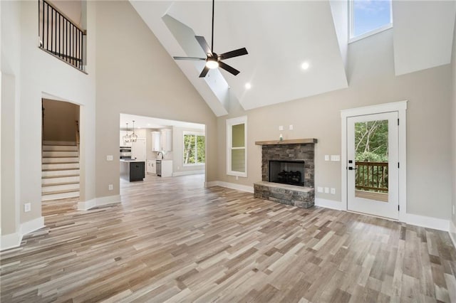 unfurnished living room with a skylight, a fireplace, ceiling fan, high vaulted ceiling, and light hardwood / wood-style flooring