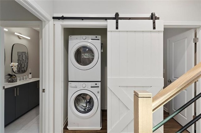 clothes washing area with a barn door, stacked washer and clothes dryer, and sink