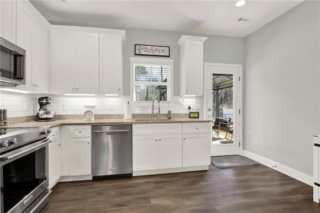 kitchen featuring tasteful backsplash, white cabinets, appliances with stainless steel finishes, light stone countertops, and a sink