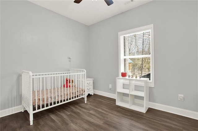 bedroom with visible vents, ceiling fan, wood finished floors, a crib, and baseboards