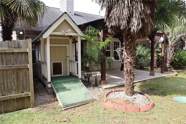 exterior space featuring fence, roof with shingles, a chimney, a yard, and a patio