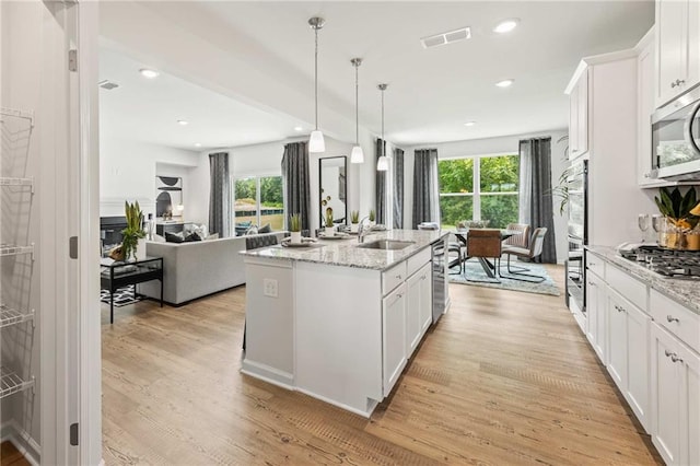 kitchen with light wood-type flooring, white cabinetry, a center island with sink, and decorative light fixtures