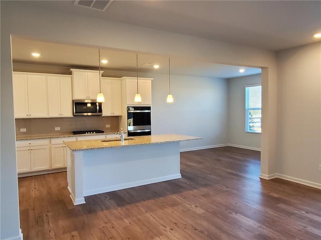 kitchen featuring appliances with stainless steel finishes, white cabinetry, dark wood-type flooring, an island with sink, and decorative light fixtures