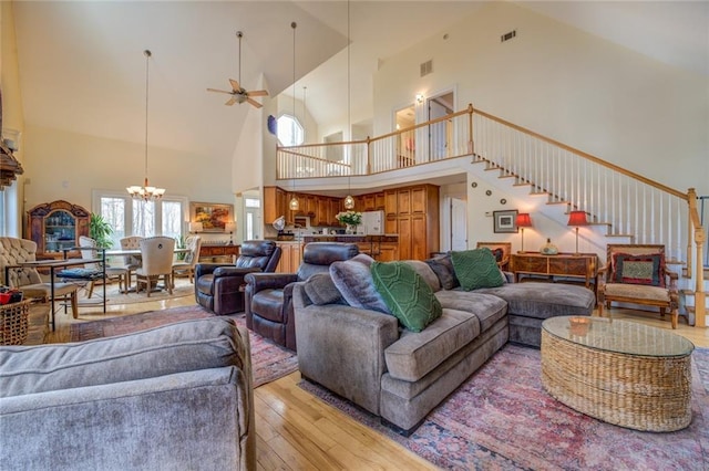 living room featuring high vaulted ceiling, light hardwood / wood-style floors, and ceiling fan with notable chandelier