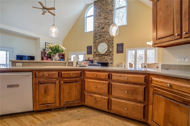 kitchen with high vaulted ceiling, ceiling fan, dishwashing machine, a stone fireplace, and light wood-type flooring