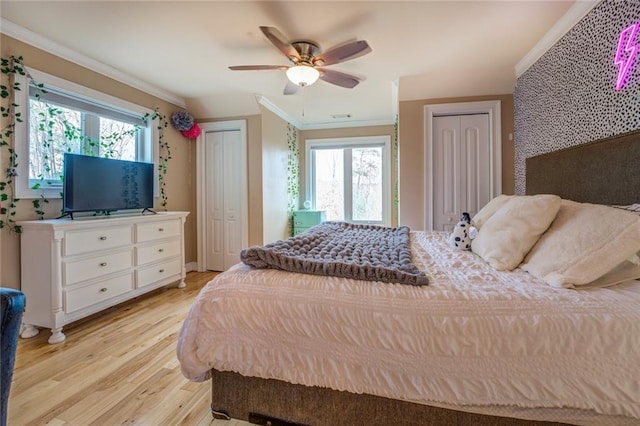 bedroom featuring multiple closets, multiple windows, light hardwood / wood-style flooring, and ornamental molding