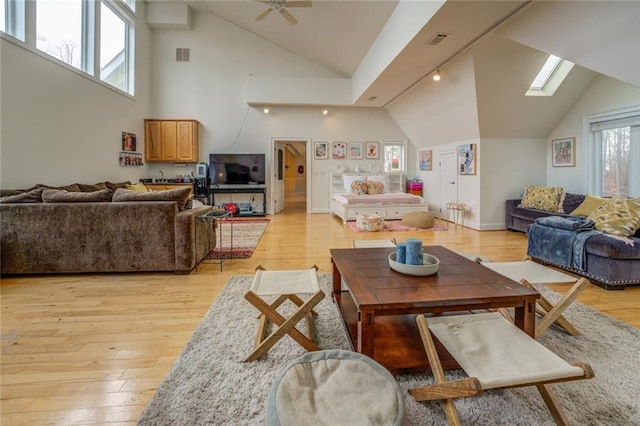 living room featuring ceiling fan, high vaulted ceiling, a skylight, and light hardwood / wood-style floors