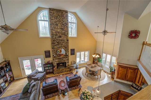 living room featuring light hardwood / wood-style flooring, a fireplace, high vaulted ceiling, and ceiling fan with notable chandelier