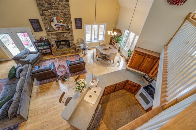 living room featuring a stone fireplace, a chandelier, a towering ceiling, and light wood-type flooring