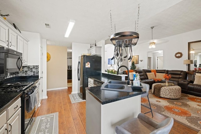 kitchen with a breakfast bar, white cabinetry, sink, black appliances, and light hardwood / wood-style flooring