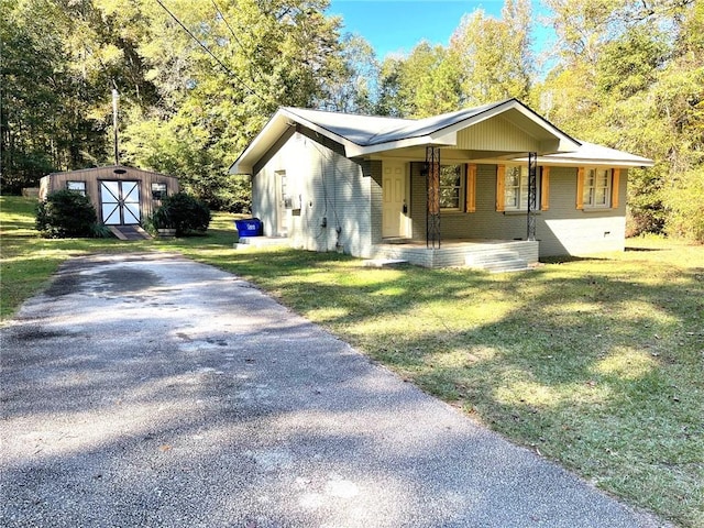 view of front of property featuring covered porch, a front lawn, and a storage shed