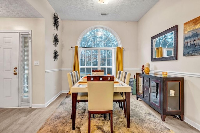 dining room featuring baseboards, light wood-style floors, visible vents, and a textured ceiling