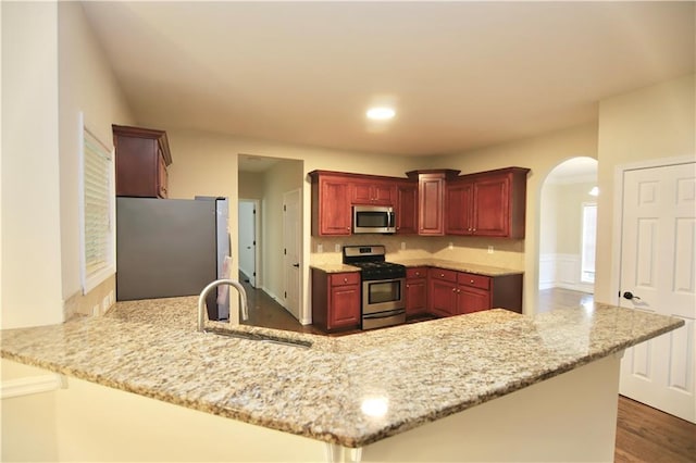 kitchen with kitchen peninsula, appliances with stainless steel finishes, light stone countertops, and sink