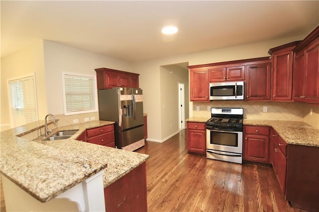 kitchen with stainless steel appliances, kitchen peninsula, dark hardwood / wood-style flooring, sink, and backsplash