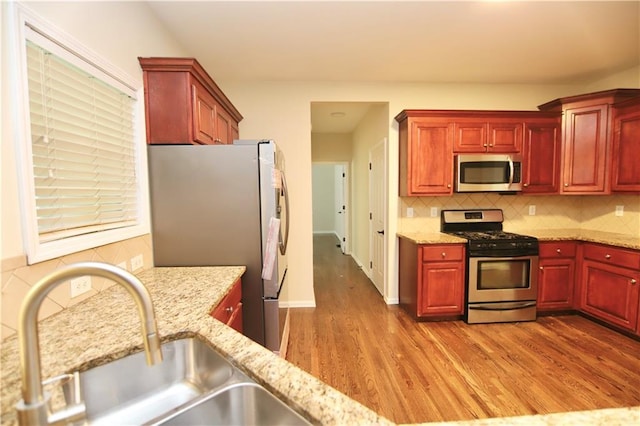 kitchen with stainless steel appliances, light stone counters, sink, light hardwood / wood-style flooring, and tasteful backsplash