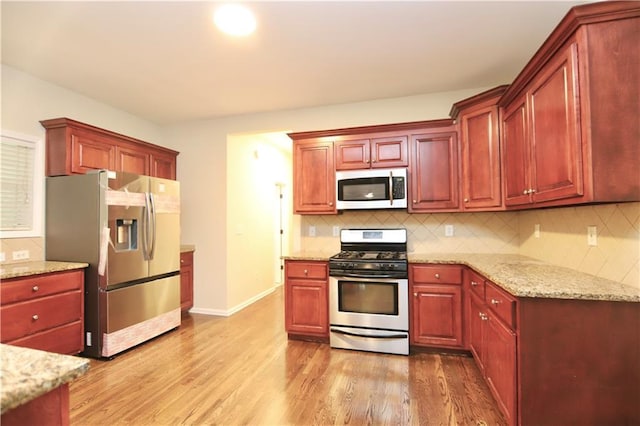 kitchen featuring stainless steel appliances, light wood-type flooring, light stone countertops, and decorative backsplash