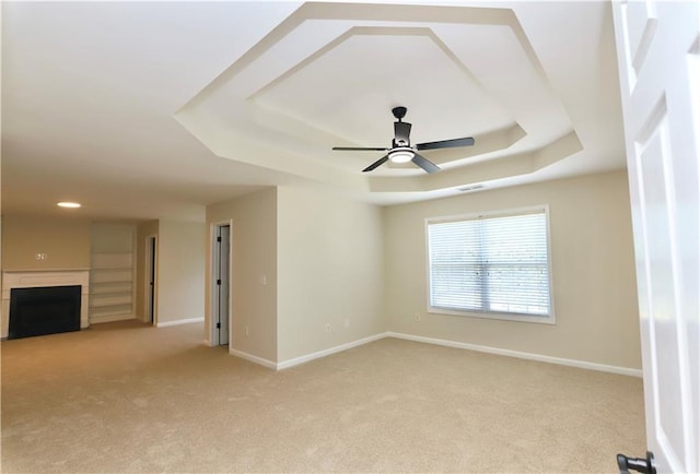 empty room with a raised ceiling, light carpet, and ceiling fan