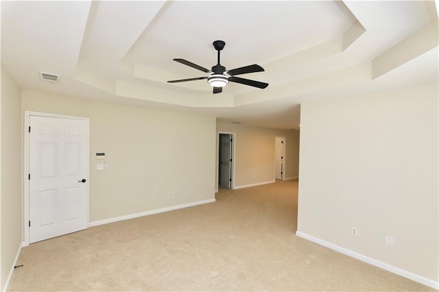 carpeted spare room featuring a raised ceiling and ceiling fan