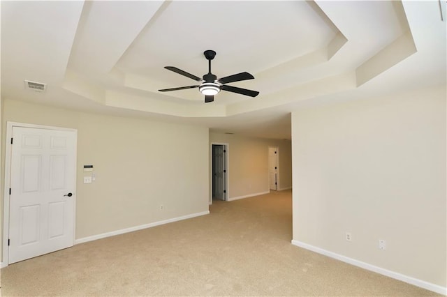 empty room featuring a raised ceiling, light colored carpet, and ceiling fan