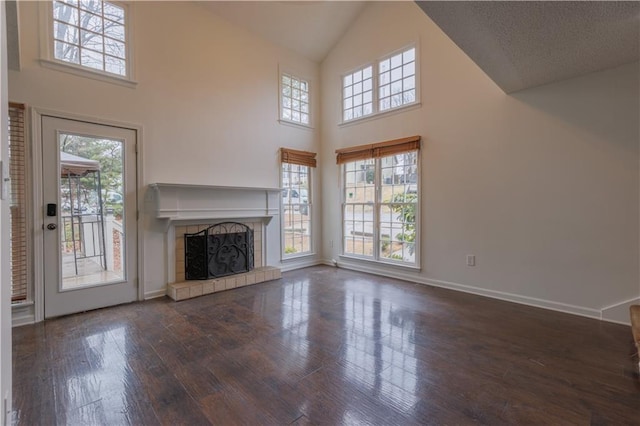 unfurnished living room with dark wood-style floors, high vaulted ceiling, a tile fireplace, and baseboards