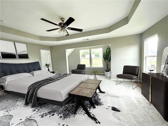 carpeted bedroom featuring multiple windows, a tray ceiling, and ceiling fan