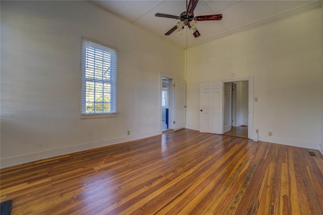 unfurnished room with dark wood-type flooring, a towering ceiling, and ceiling fan