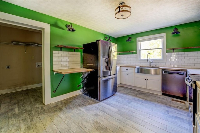 kitchen featuring sink, butcher block countertops, white cabinetry, stainless steel appliances, and light hardwood / wood-style flooring