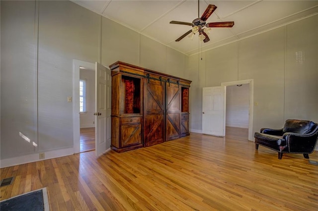 interior space with ceiling fan, a barn door, light hardwood / wood-style flooring, a towering ceiling, and crown molding