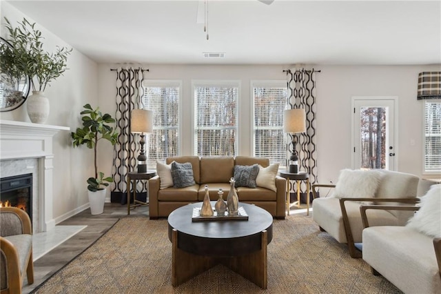 living room with ceiling fan, a premium fireplace, baseboards, wood finished floors, and visible vents