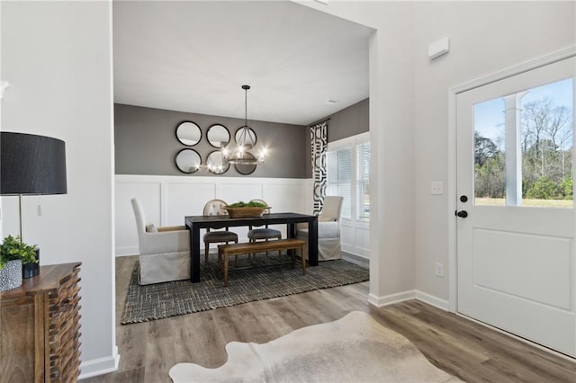 foyer with a notable chandelier, wainscoting, wood finished floors, and a decorative wall