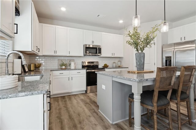 kitchen featuring tasteful backsplash, a sink, a breakfast bar, stainless steel appliances, and light wood-style flooring