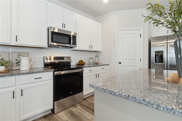 kitchen featuring appliances with stainless steel finishes, light stone counters, white cabinetry, decorative backsplash, and wood finished floors